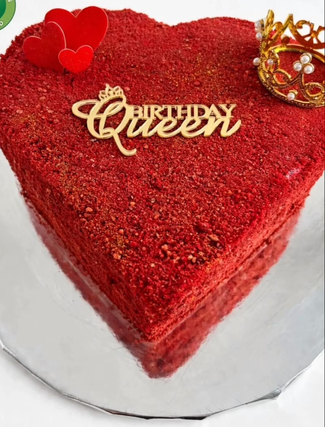 A red heart-shaped cake with a gold crown and Queen topper by Britanade Cakes